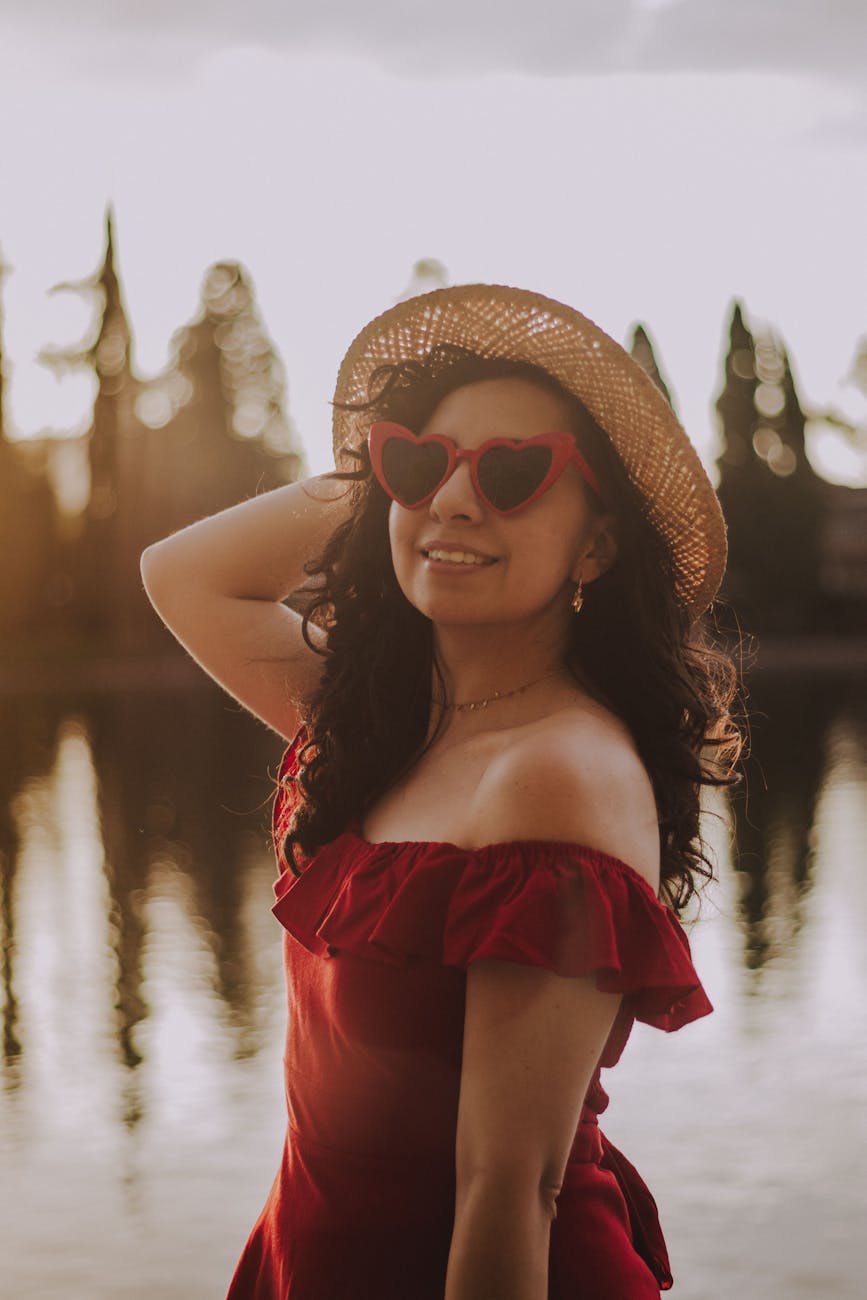 woman in red off shoulder dress wearing brown sun hat and black sunglasses